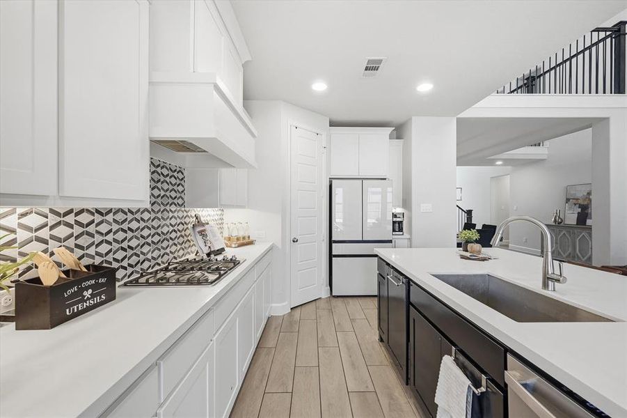 Kitchen with two tone cabinets, wood tiled floors, stainless steel appliances, light stone counters, and recessed lighting