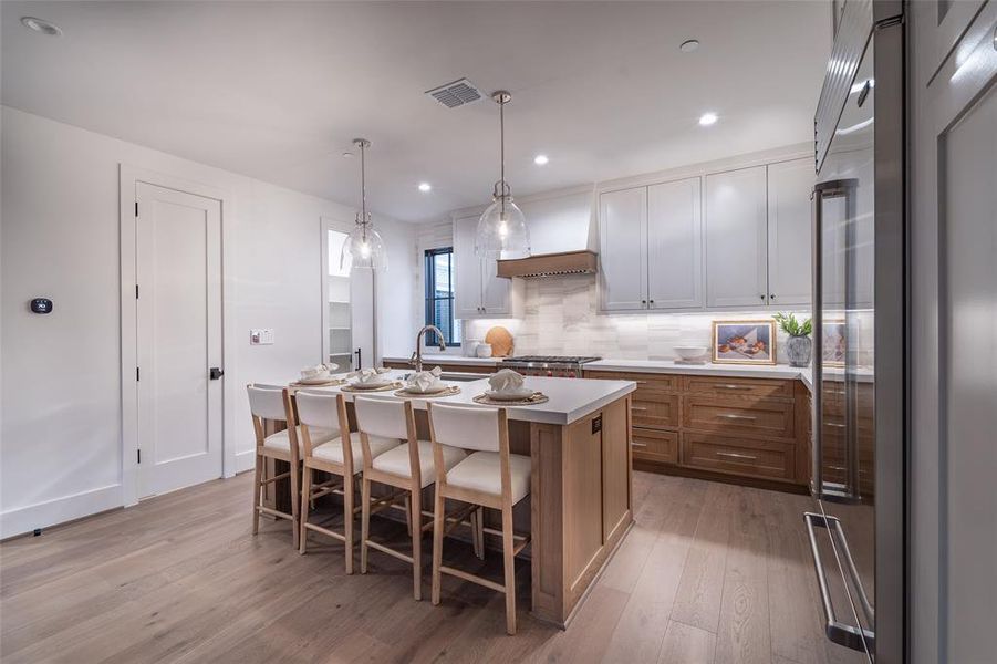 Kitchen featuring custom exhaust hood, a kitchen breakfast bar, stainless steel built in fridge, pendant lighting, and a kitchen island with sink