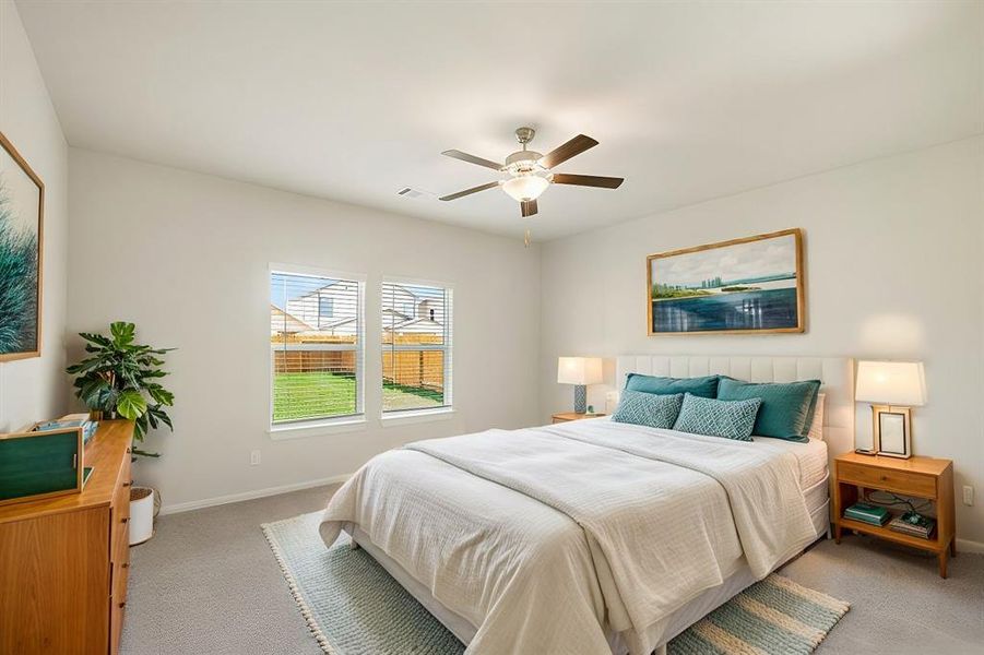 Retreat to the tranquil primary bedroom featuring plush carpeting, a ceiling fan, and soft natural light from large windows. The attached en-suite bath enhances privacy and convenience, creating a cozy sanctuary to relax and unwind.