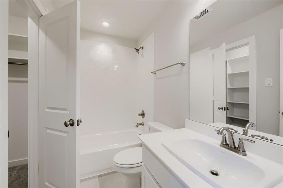 Bathroom featuring a white vanity with an integrated sink and brushed nickel faucet, a white toilet, and a bathtub with white subway tile surround