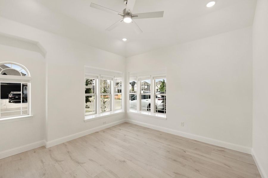 Empty room with light wood floors, ceiling fan, and large windows with neighborhood views