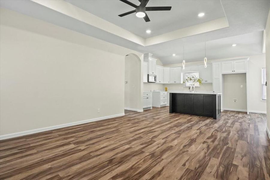 Unfurnished living room featuring arched walkways, dark wood finished floors, a tray ceiling, recessed lighting, and a ceiling fan Unfurnished living room featuring arched walkways, dark wood finished floors, a tray ceiling, recessed lighting, and a ceiling fan