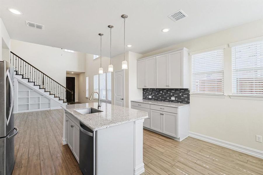 Kitchen with white cabinets, sink, hanging light fixtures, and an island with sink