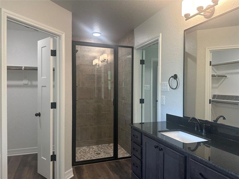 Bathroom with a walk in closet, a stall shower, wood finished floors, and a textured wall