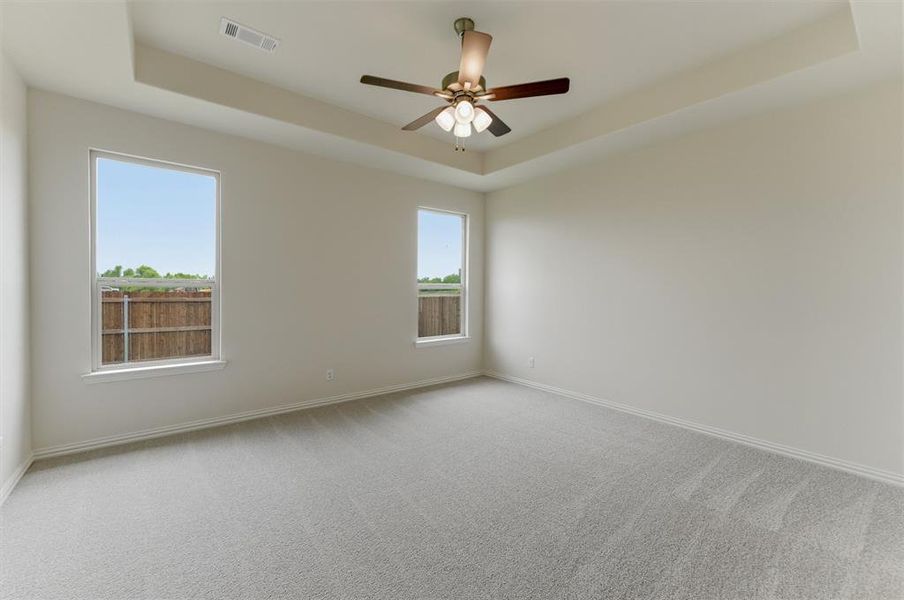 Spacious interior room featuring a tray ceiling with a ceiling fan, two large windows, light-toned carpeting, and neutral wall tones