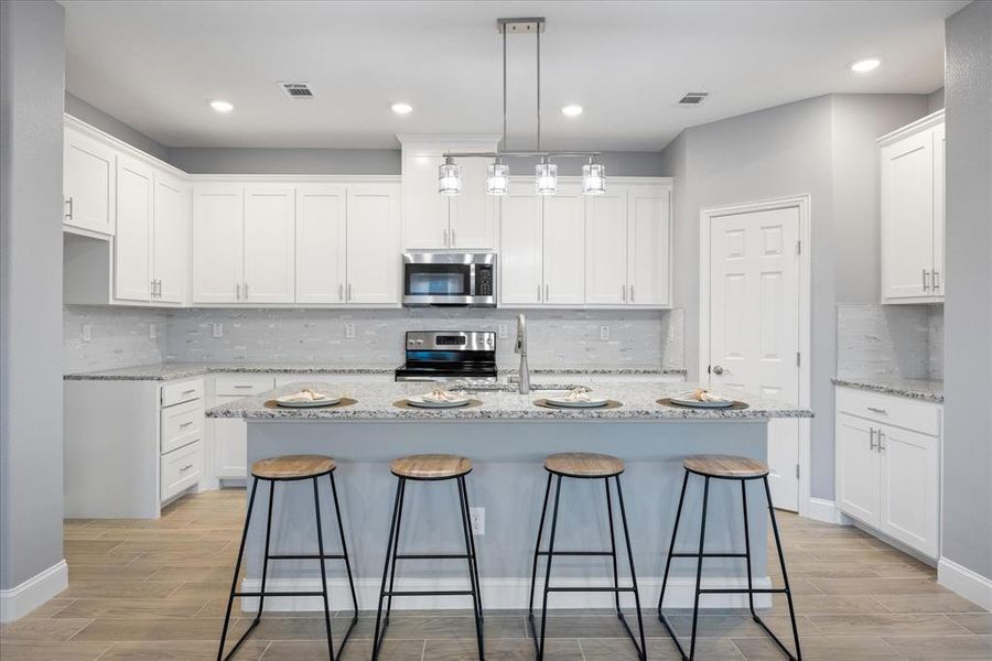 Kitchen with white cabinets, stainless steel appliances, a kitchen island with sink, and decorative light fixtures