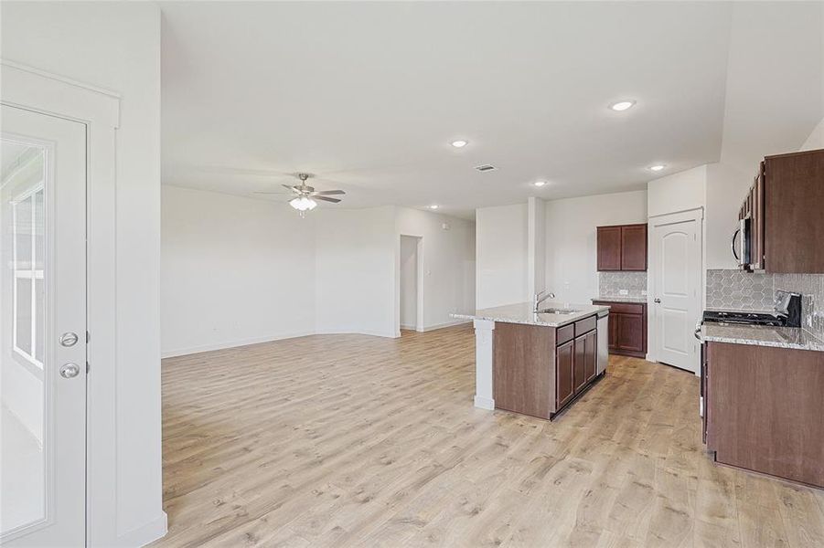 Kitchen with decorative backsplash, light wood-type flooring, light stone counters, ceiling fan, and a center island with sink