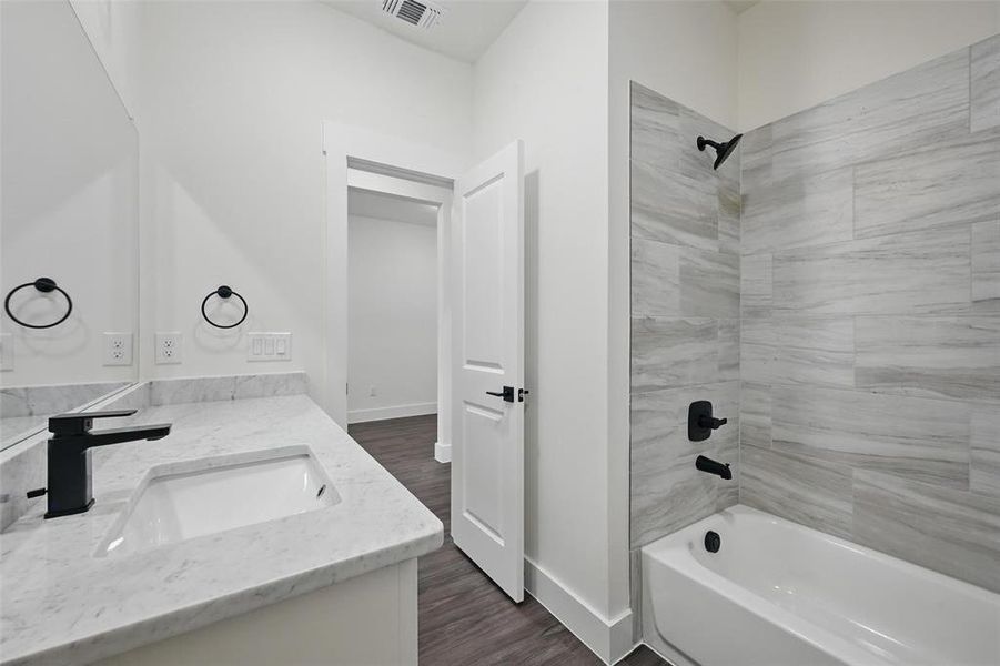 Full bathroom with tub / shower combination, a sink, visible vents, double vanity, and wood finished floors Full bathroom with tub / shower combination, a sink, visible vents, double vanity, and wood finished floors