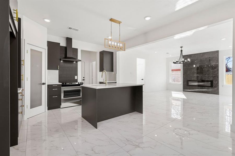 Kitchen featuring wall chimney exhaust hood, decorative light fixtures, a fireplace, sink, and a kitchen island with sink