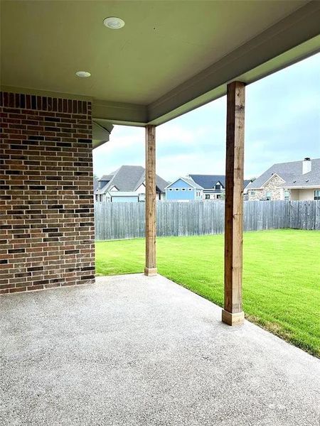 Covered patio with a textured concrete surface, supported by two wooden posts Covered patio with a textured concrete surface, supported by two wooden posts