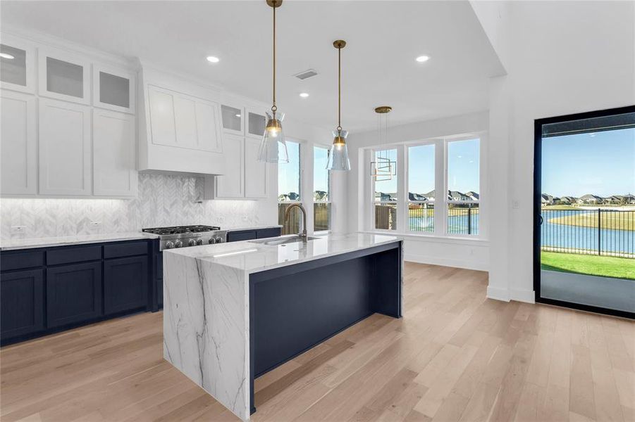 Kitchen with white cabinetry, backsplash, light wood finished floors, glass insert cabinets, and decorative light fixtures
