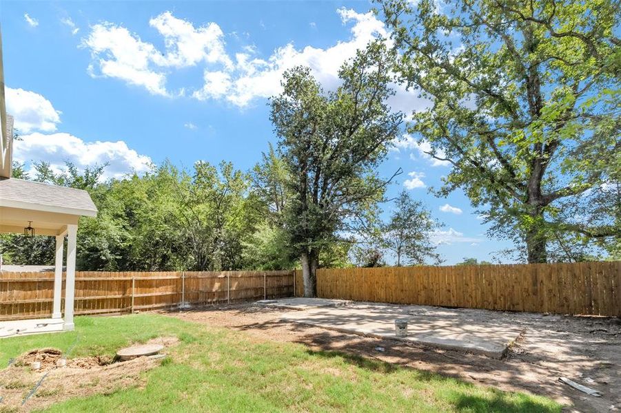 Expansive backyard featuring a partial concrete slab, wood privacy fencing, and mature trees Expansive backyard featuring a partial concrete slab, wood privacy fencing, and mature trees