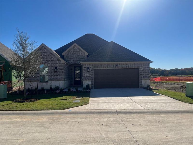 View of beautiful brick and stone front facade just completed October 16, 2024 with a front yard that is always mowed and landscaped by your HOA and an oversized 2 car garage.