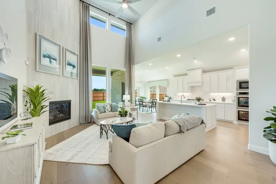 Open-concept living room with two-story ceiling, fireplace, and kitchen visible in background