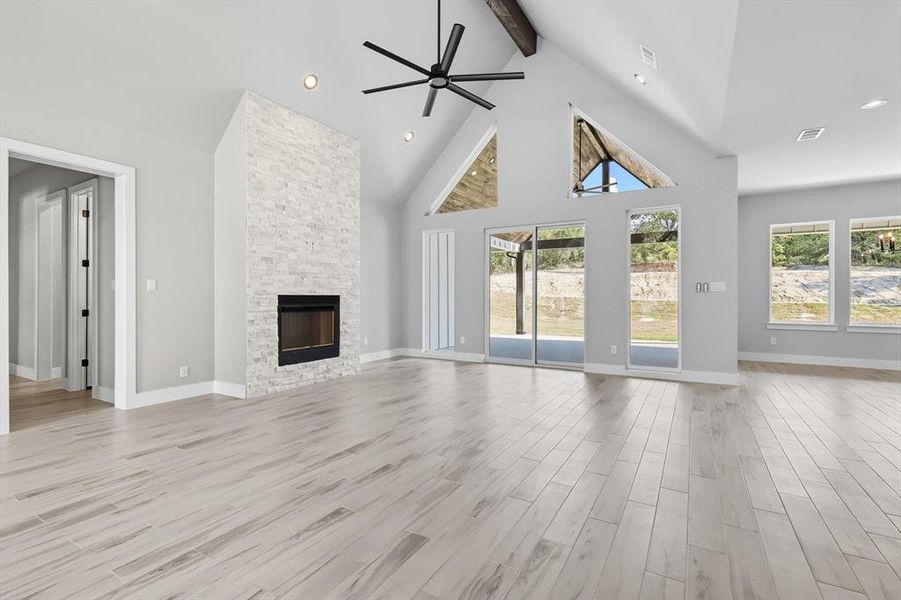 Unfurnished living room featuring beamed ceiling, high vaulted ceiling, a ceiling fan, light wood-type flooring, and a stone fireplace Unfurnished living room featuring beamed ceiling, high vaulted ceiling, a ceiling fan, light wood-type flooring, and a stone fireplace