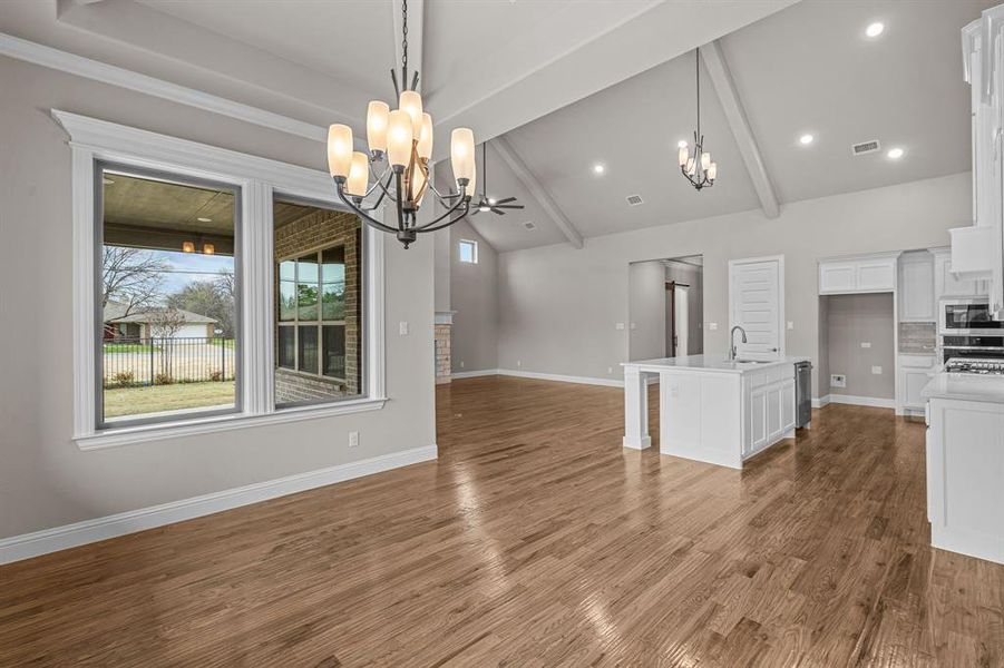 Unfurnished dining area with an inviting chandelier, hardwood / wood-style floors, vaulted ceiling with beams, and sink. Not actual home. Previous built example.