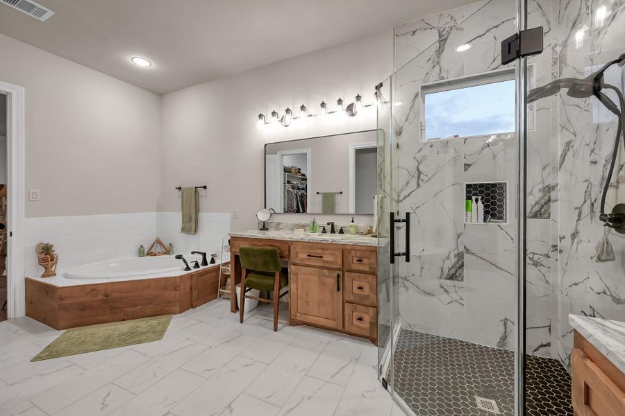 This modern bathroom features a spacious layout with a luxurious soaking tub, a large glass-enclosed shower and dual vanities with wooden cabinetry.