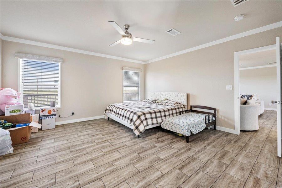 Primary bedroom featuring wood tiled floors, ornamental molding, and a ceiling fan Primary bedroom featuring wood tiled floors, ornamental molding, and a ceiling fan
