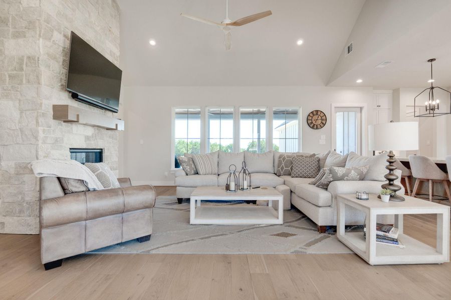 Living room with light wood-style floors, ceiling fan, a fireplace, hanging lights, and lofted ceiling