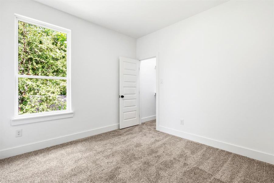 Neutral white walls with crisp white trim, a large window, light-colored carpet, and a modern five-panel interior door Neutral white walls with crisp white trim, a large window, light-colored carpet, and a modern five-panel interior door