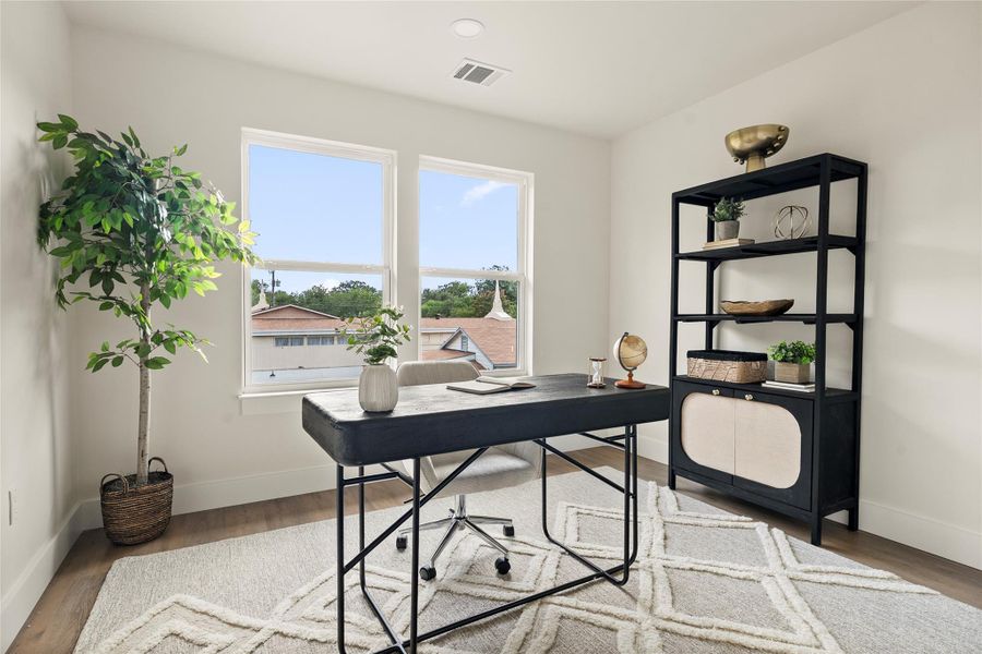 Well-lit study with recessed lighting and two large windows framing neighborhood views, offering a quiet retreat.