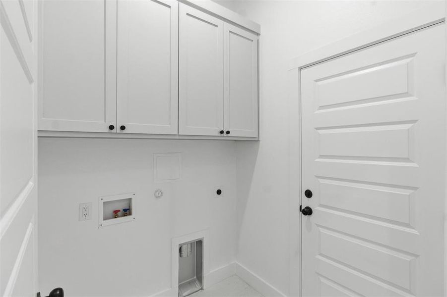Bright laundry space featuring white shaker-style cabinetry with black hardware, a multi-panel interior door with black hardware, and utility hookups