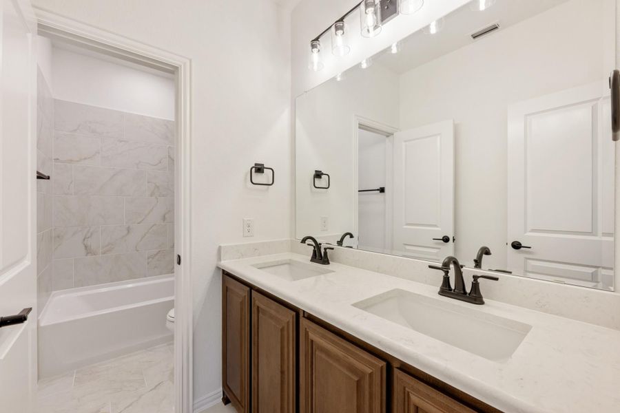 Bathroom with double sink vanity, wood cabinets, white countertops, and tiled shower with tub combo