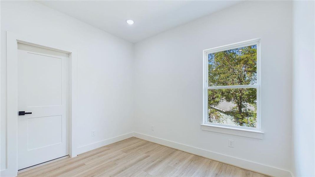 The spacious secondary bedroom features wood-look LVP flooring, recessed lighting, and a large window that fills the room with natural light.