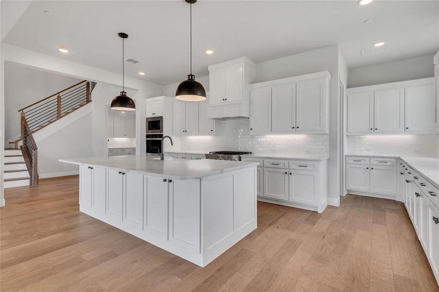 Kitchen featuring pendant lighting, a kitchen island with sink, white cabinetry, light wood-type flooring, and decorative backsplash