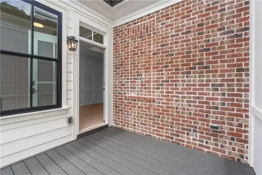 Exterior porch with grey composite decking, multi-tone brick facade, white siding, and black-framed window