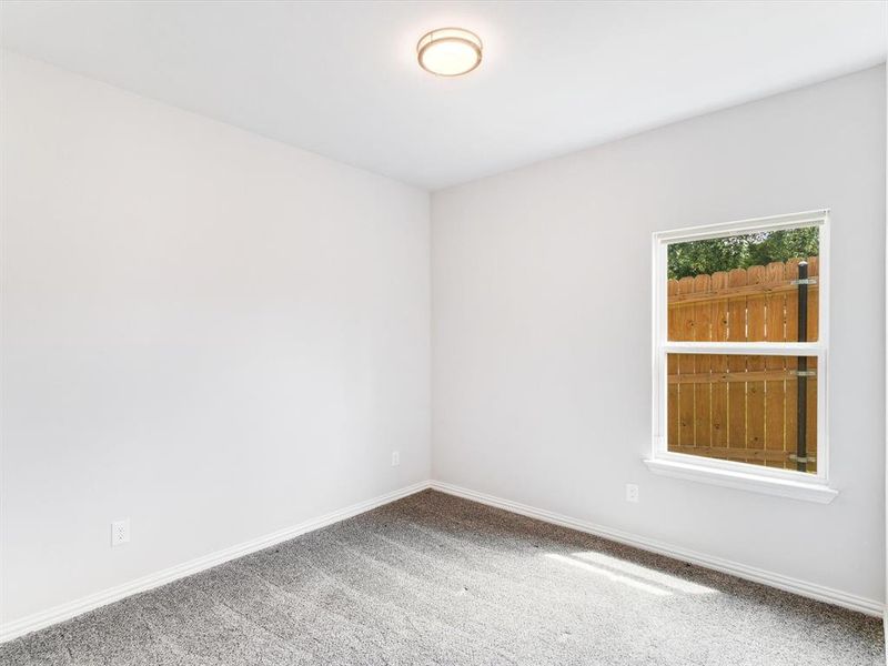 Bright interior room featuring a single window, overhead flush-mount lighting, light gray wall paint, white baseboards, and gray textured carpeting