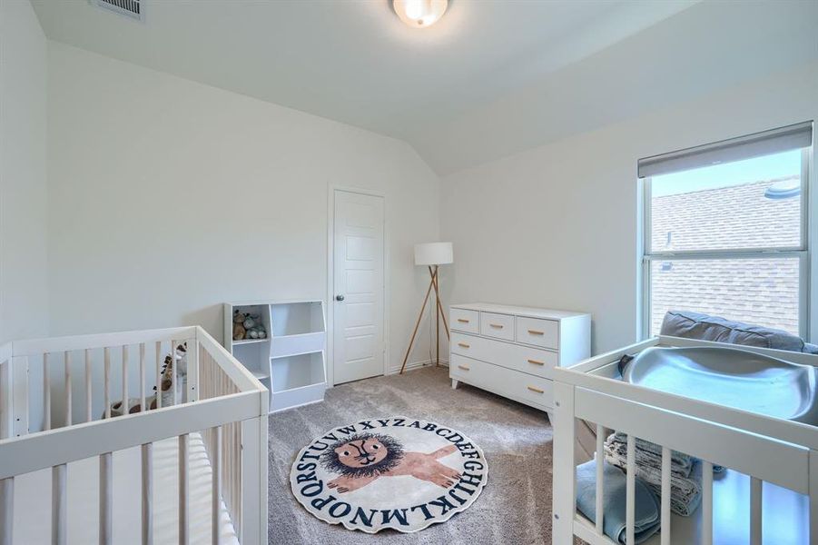 Carpeted bedroom featuring a nursery area and lofted ceiling