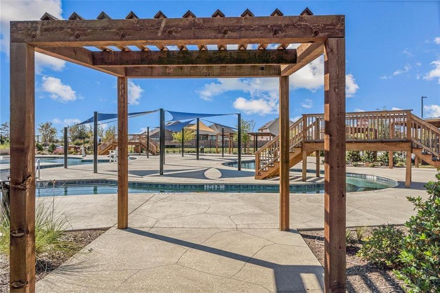 Community swimming pool area featuring multiple pools, a wooden pergola, shade sails, and an elevated wooden deck with stairs Community swimming pool area featuring multiple pools, a wooden pergola, shade sails, and an elevated wooden deck with stairs