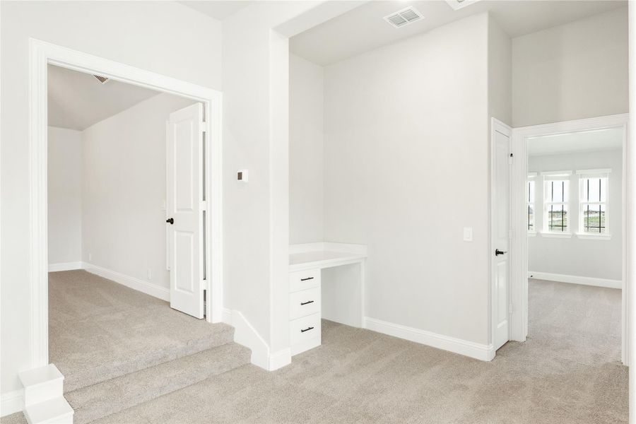 Upstairs hallway with built-in desk, carpet flooring, and doorways leading to multiple rooms Upstairs hallway with built-in desk, carpet flooring, and doorways leading to multiple rooms