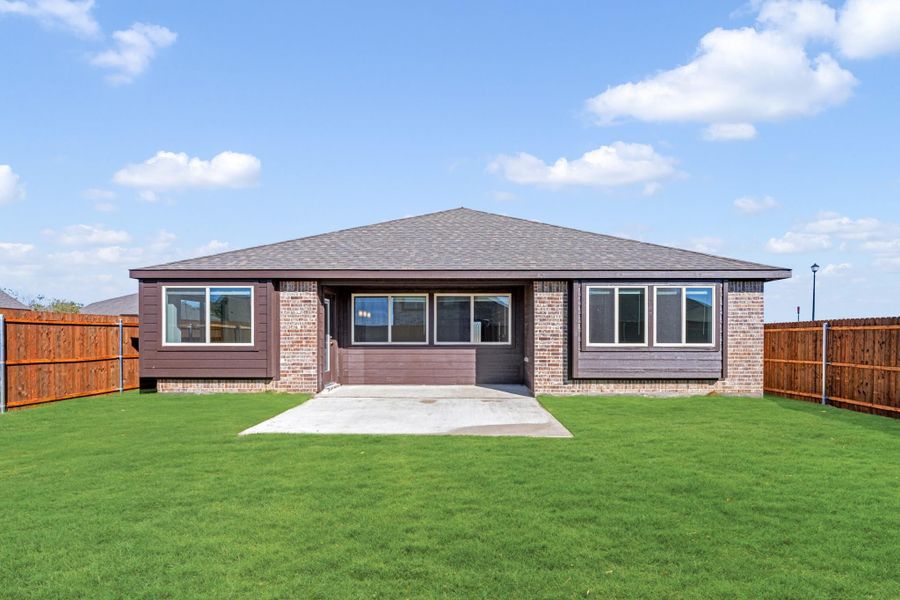 Rear exterior of single-story brick home with covered patio, green lawn, and wood privacy fence