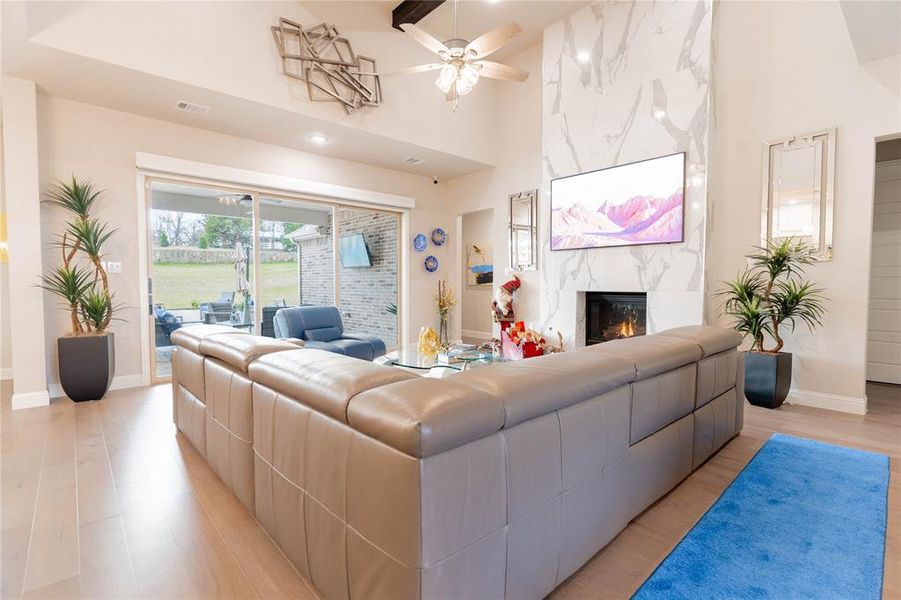 Living room with a fireplace, a ceiling fan, light wood-style flooring, and high vaulted ceiling