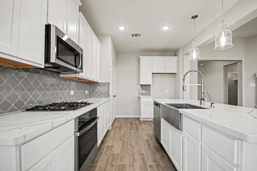 Sleek modern kitchen with white cabinetry, stainless steel appliances, and a stylish backsplash, complemented by elegant pendant lighting over a spacious island.