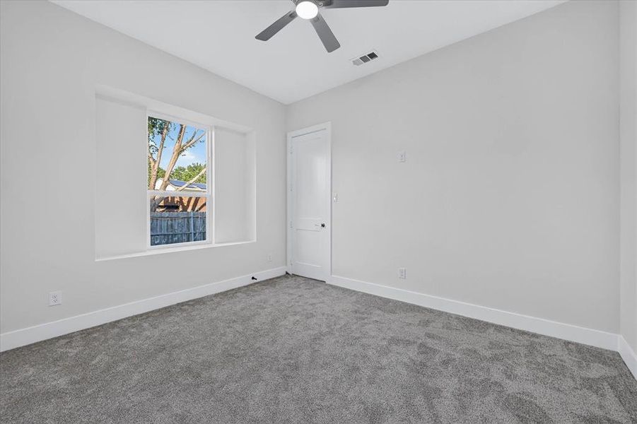 Neutral gray carpeting complemented by white baseboards, a white door with a dark knob, and a window framing exterior greenery Neutral gray carpeting complemented by white baseboards, a white door with a dark knob, and a window framing exterior greenery