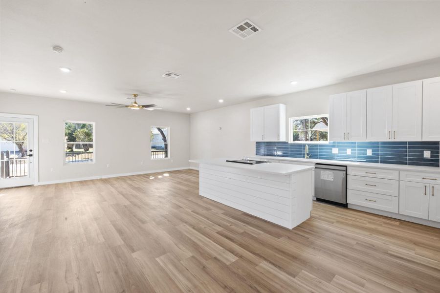 Kitchen featuring white cabinets, a kitchen island, backsplash, stainless steel dishwasher, and light wood-style floors Kitchen featuring white cabinets, a kitchen island, backsplash, stainless steel dishwasher, and light wood-style floors