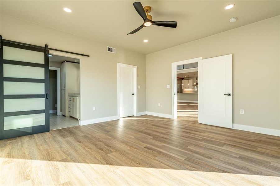 Unfurnished bedroom with a barn door, light wood-style floors, ensuite bath, recessed lighting, and ceiling fan Unfurnished bedroom with a barn door, light wood-style floors, ensuite bath, recessed lighting, and ceiling fan