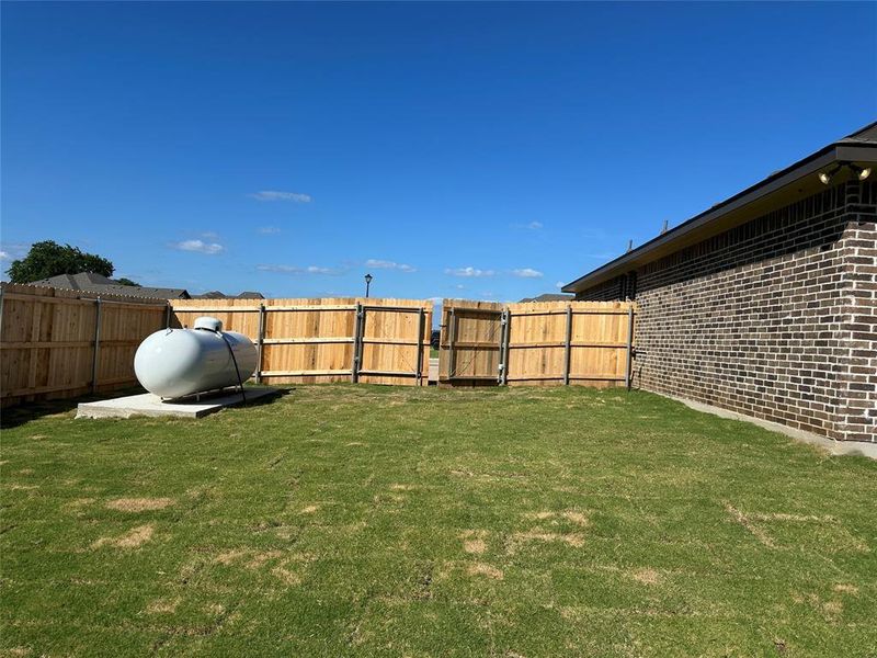 Expansive backyard featuring a manicured lawn, full privacy fencing with double gate access, and a brick exterior