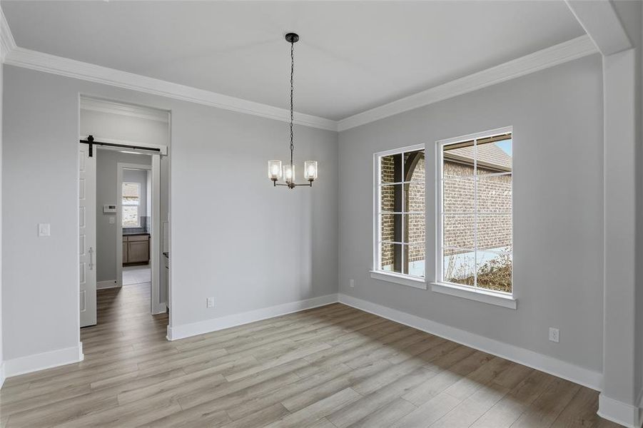Unfurnished dining area featuring a barn door, ornamental molding, light wood-style floors, and hanging lights