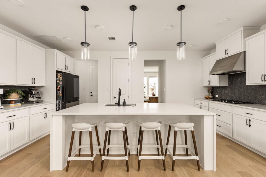 Kitchen featuring a central island with integrated sink, white cabinetry with black hardware, and wood-finish flooring