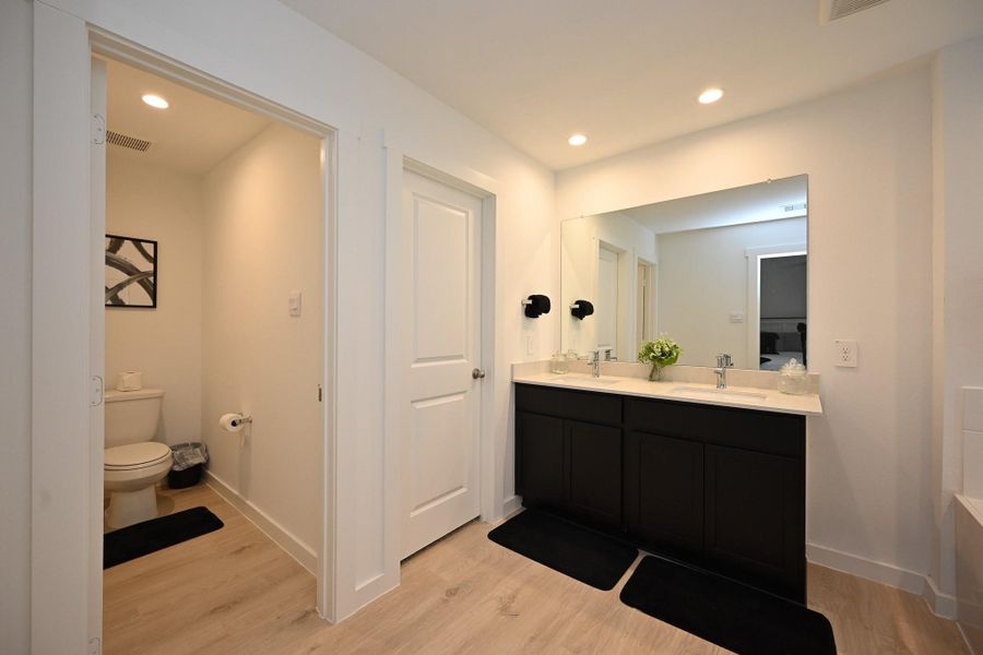 The primary ensuite bath has dual sinks and a large mirror. It has a separate toilet area and stylish lighting, complimented by light wood flooring and dark cabinetry for a sleek, contemporary look. The primary ensuite bath has dual sinks and a large mirror. It has a separate toilet area and stylish lighting, complimented by light wood flooring and dark cabinetry for a sleek, contemporary look.