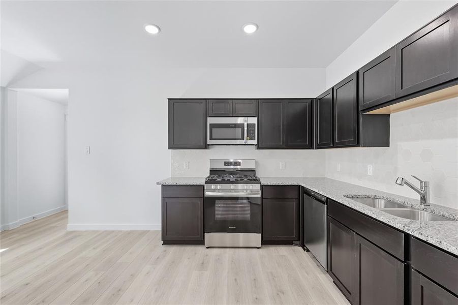 Kitchen featuring stainless steel appliances, light stone counters, light wood-style floors, and recessed lighting Kitchen featuring stainless steel appliances, light stone counters, light wood-style floors, and recessed lighting