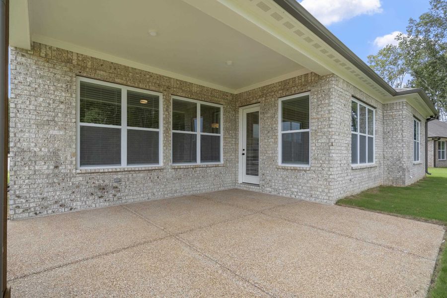 Covered patio featuring an exposed aggregate concrete surface, brick exterior, and multiple windows