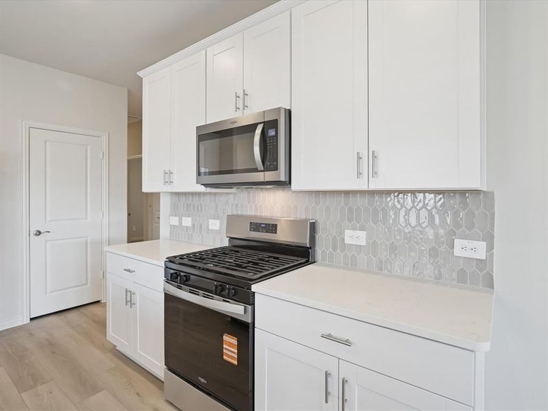 Kitchen featuring stainless steel appliances, white cabinets, decorative backsplash, and light wood finished floors