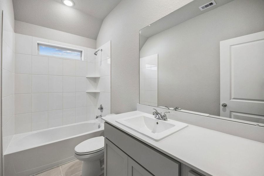 A well-appointed bathroom offers a clean aesthetic with a bright vanity and a tiled shower-tub combination.