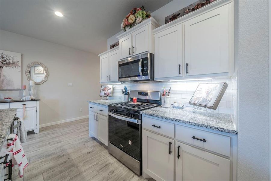 Kitchen featuring white cabinets, light hardwood / wood-style flooring, tasteful backsplash, light stone counters, and stainless steel appliances