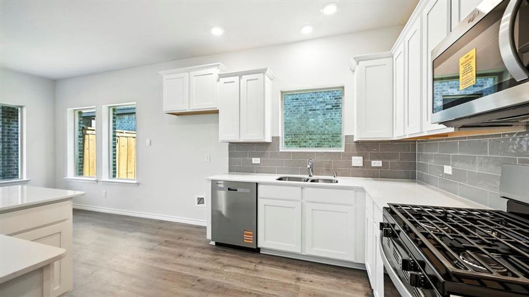 Kitchen featuring stainless steel appliances, white cabinetry, light wood-type flooring, decorative backsplash, and light stone countertops